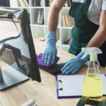 cropped shot of professional cleaner in rubber gloves cleaning computer keyboard in office