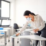 Teacher back at school after covid-19 quarantine and lockdown, disinfecting desks